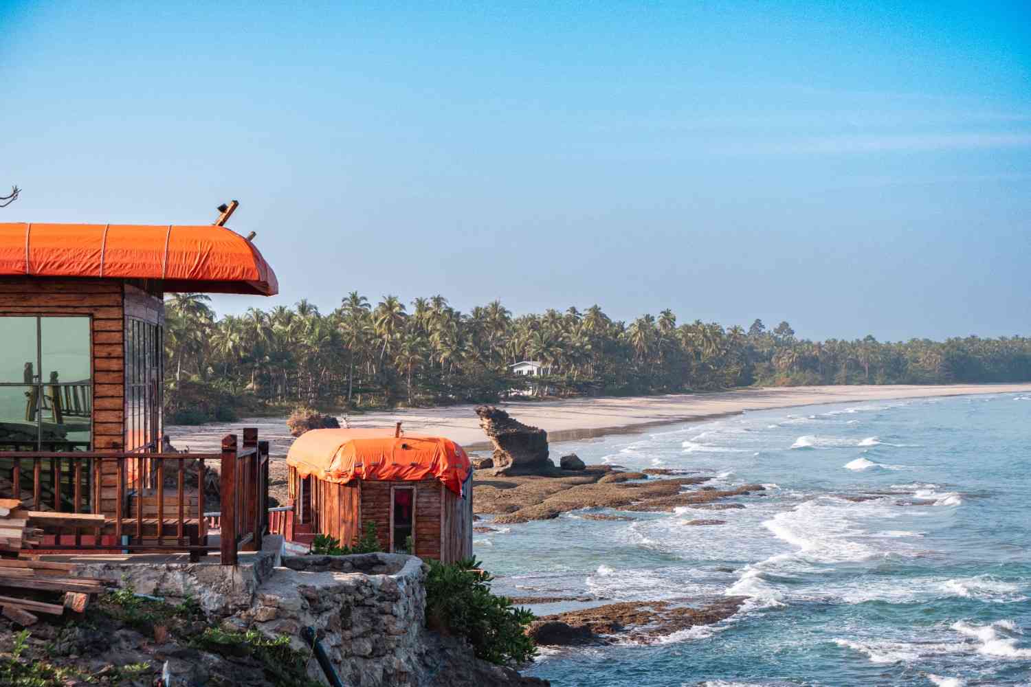 A scenic coastal view with wooden beach huts topped with orange canopies overlooking rocky shores and gentle waves, creating a relaxing beachside atmosphere that reflects some of the best Things to do in Panjim.