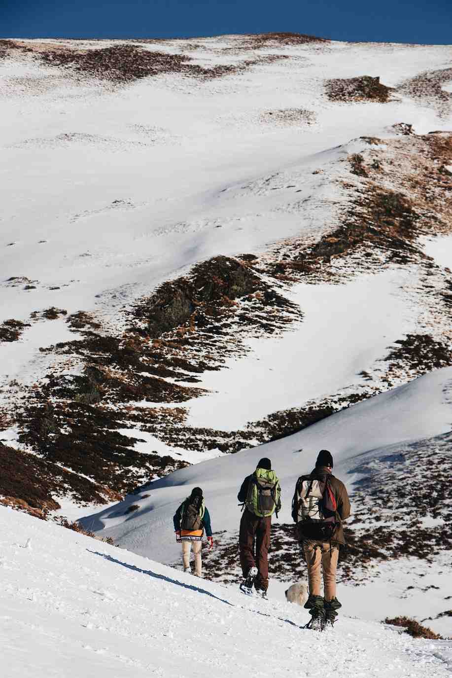 Trekking group walking uphill across a snowy mountain slope surrounded by rugged terrain, capturing the raw adventure of winter treks in India.