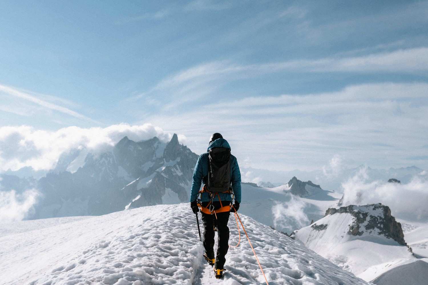 A mountaineer walking along a snowy high-altitude ridge surrounded by dramatic alpine peaks and clouds, reflecting the adventure and challenge of the best winter treks