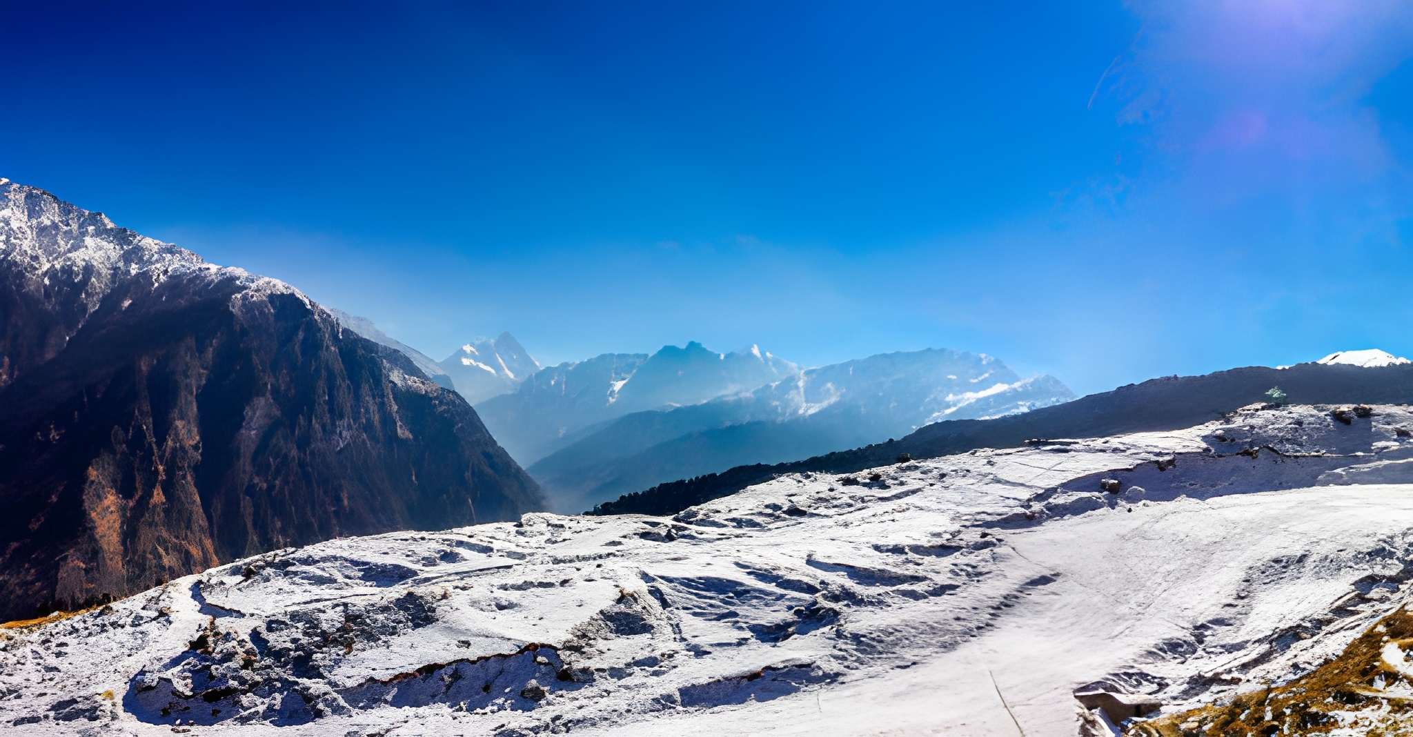 Sun-lit Himalayan mountain peaks and a snow-covered ridge under a vibrant blue sky, layered valleys fading into the distance one of the Best places to see snow in India, capturing the charm of a Top Snowfall Destinations winter view.