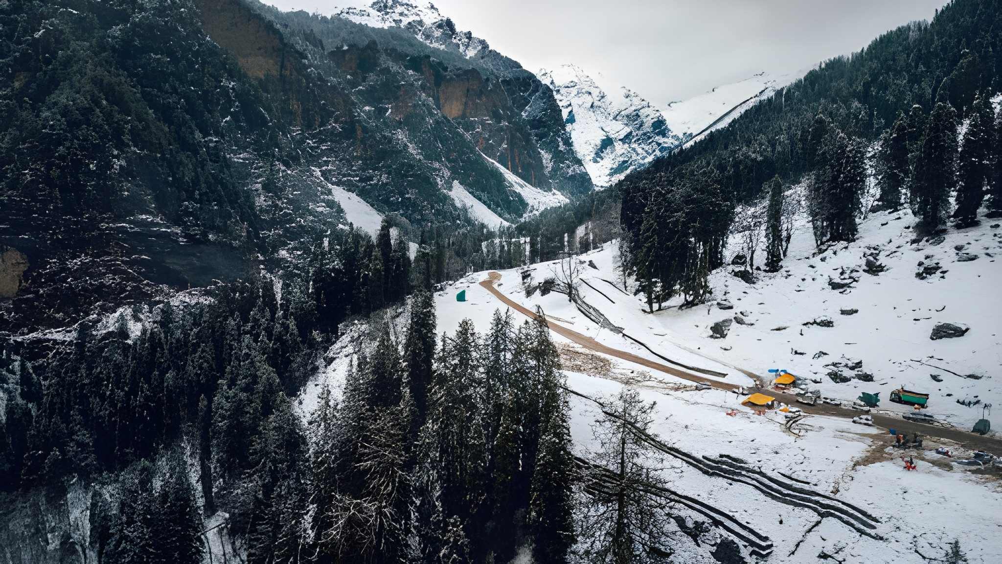 Aerial view of a Himalayan valley with snow-covered mountains, dense pine forests, and a winding road passing through the winter landscapeone of the most scenic Winter travel destinations in India and a true example of Top Snowfall Destinations charm.