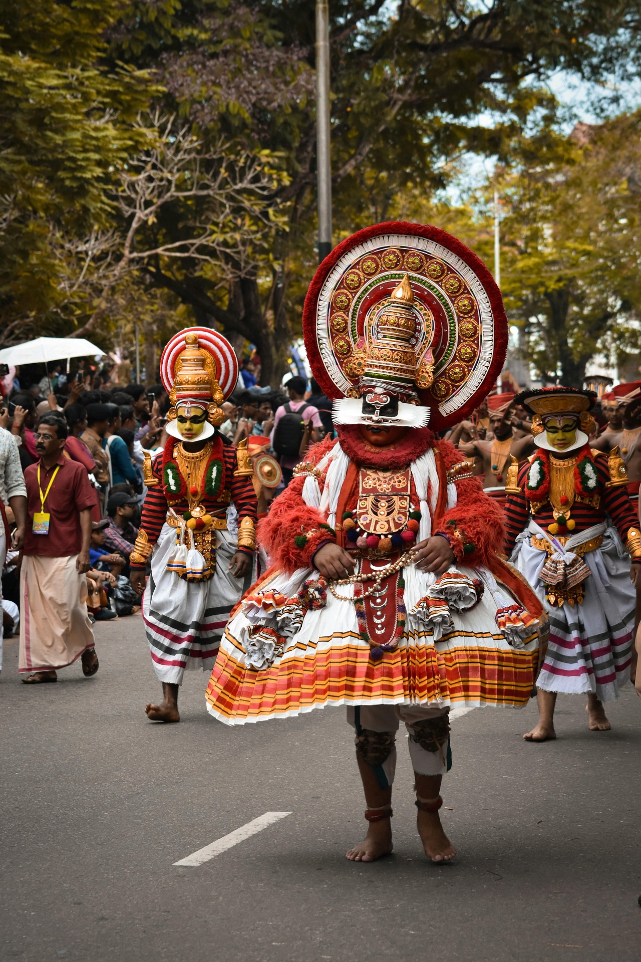 Colorful traditional dancers in tribal costumes and large decorative headgear performing in a street procession, showing the spirit of a festival in December in India.