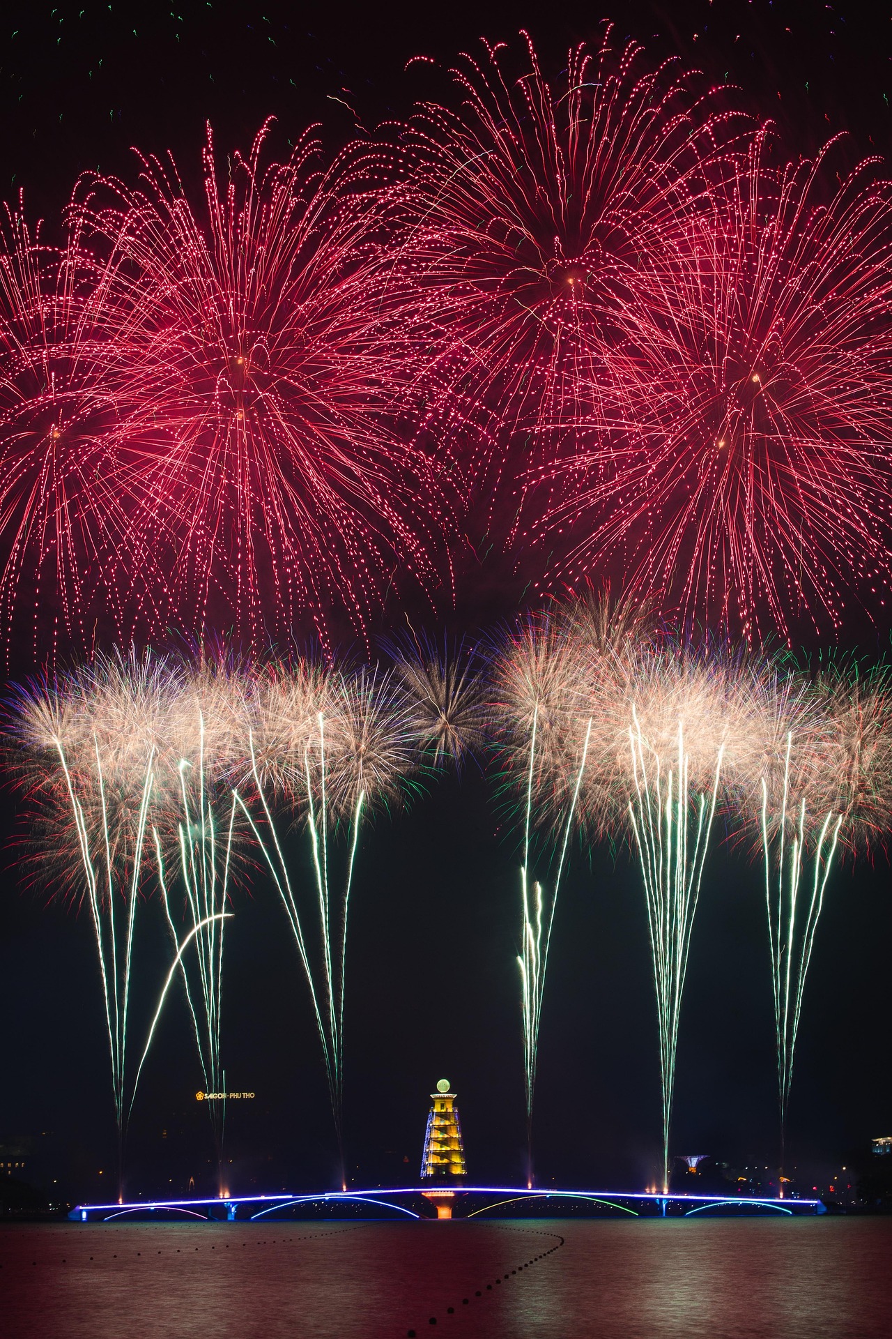Bright red and gold fireworks over a lit tower and bridge at night, capturing the energy of festivals in December.