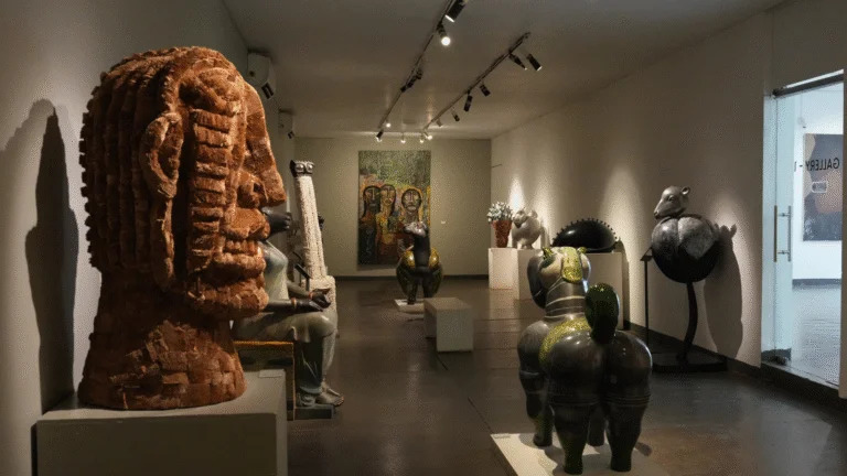 A dimly lit art gallery featuring large sculptural pieces, textured busts, and contemporary artwork arranged along a narrow hall, capturing the creative atmosphere found in many Museums in Goa.