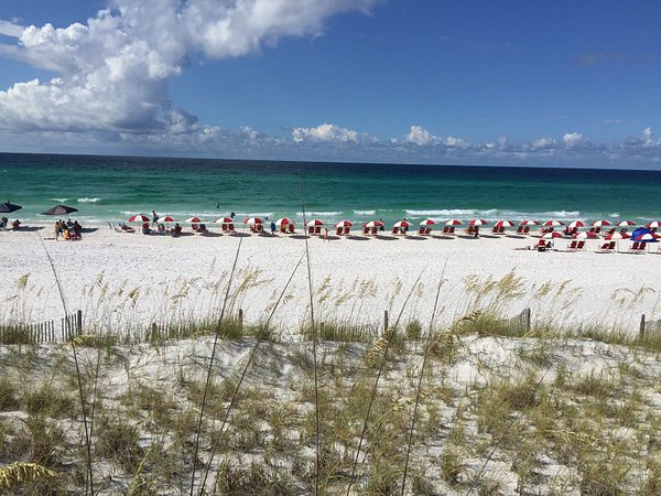 A serene sandy beach with rows of red-and-white umbrellas lined up along the shoreline, overlooking clear turquoise water, offering a relaxing coastal experience among the Things to do in Panjim.