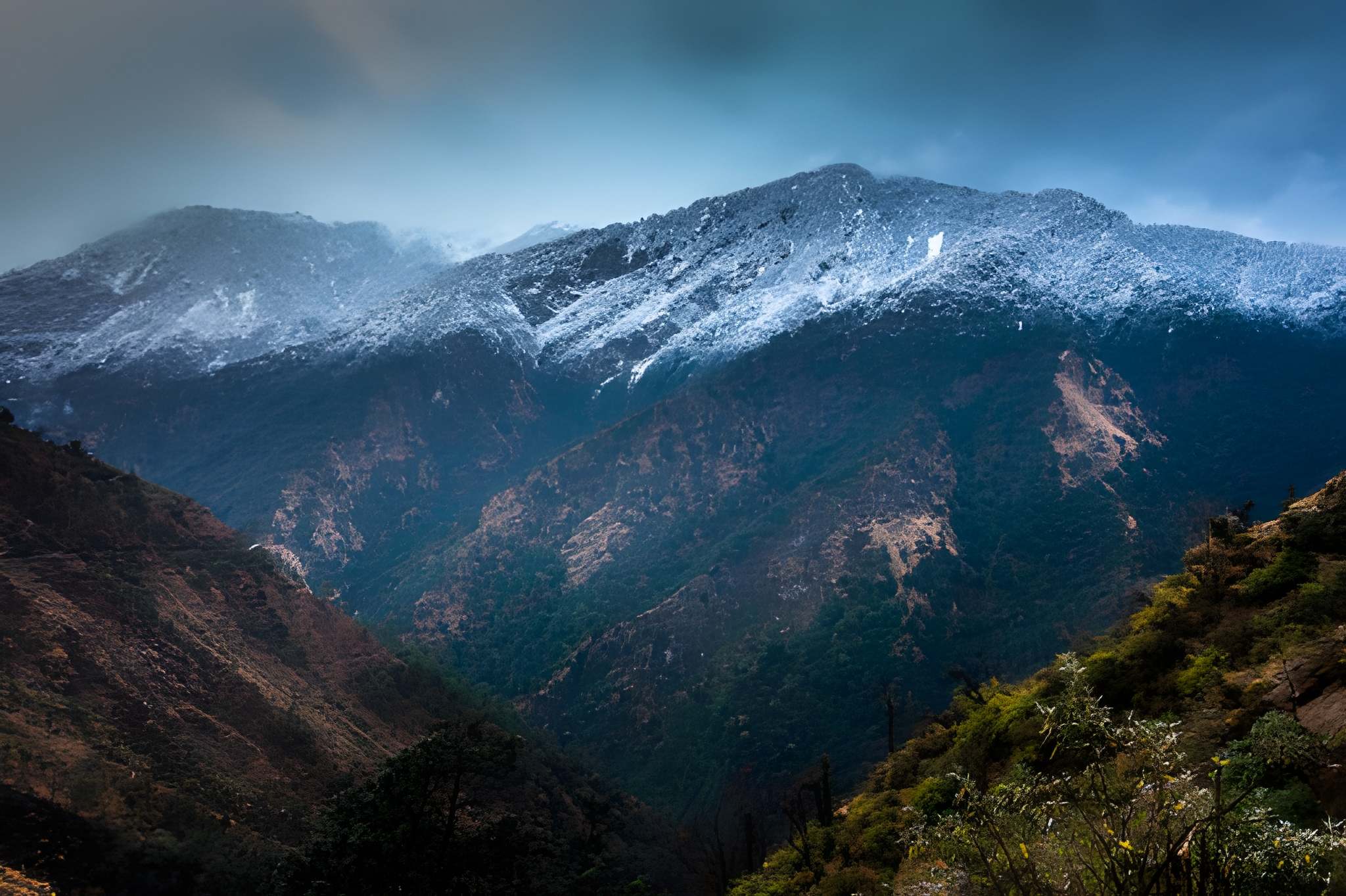 Distant mountains with light snow on their upper slopes under a cloudy sky, showing the early winter charm of snowfall in India in January.