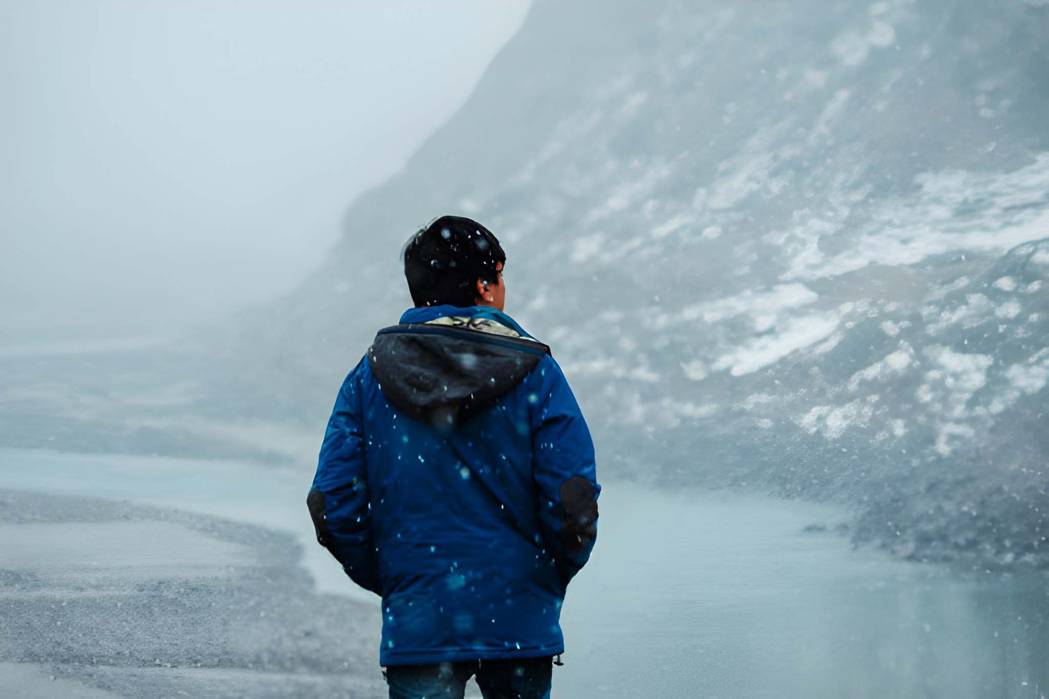 A person in a blue jacket walking beside a frozen landscape during gentle snowfall, capturing the quiet atmosphere of December snowfall in India.