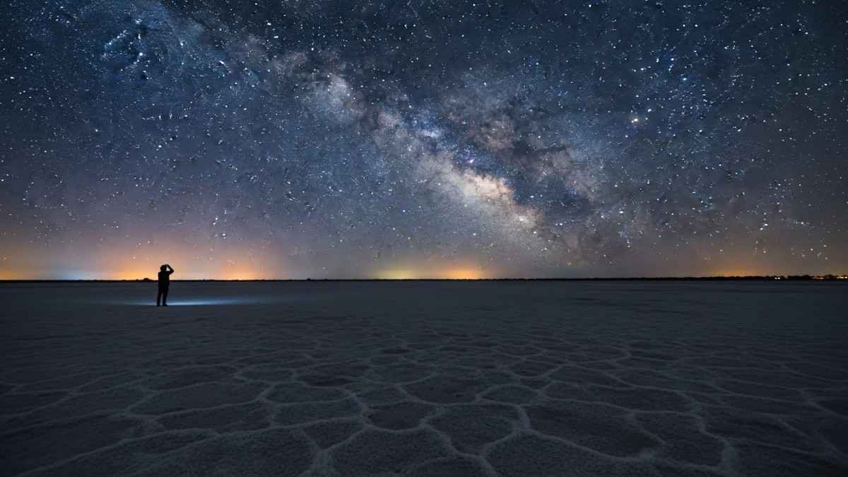 Person standing on salt flats under vast night sky, stargazing in India