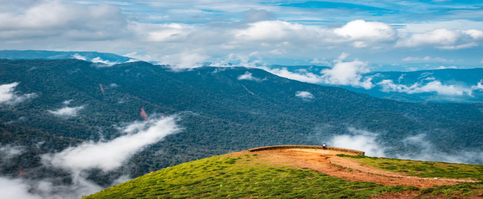 Panoramic hilltop viewpoint overlooking dense green forests and floating clouds across the valley, one of the best hill stations in India in summer for scenic views – Towno