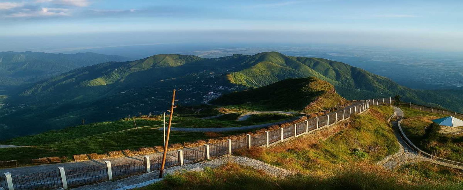 Winding mountain road passing through rolling green hills and valleys under soft sunlight, a peaceful landscape among summer hill stations in India – Towno
