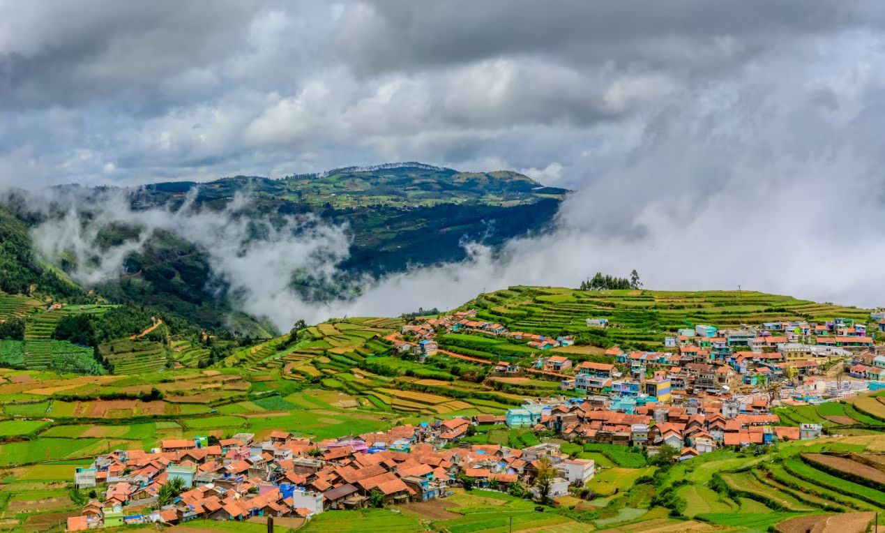 Terraced green fields and a hillside town surrounded by misty mountains in ooty, a scenic destination for India travel in April – Towno